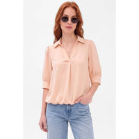 A woman wearing a Naked Zebra - Half Sleeve Hi-lo Bubble Hem Blouse in peach and blue jeans.