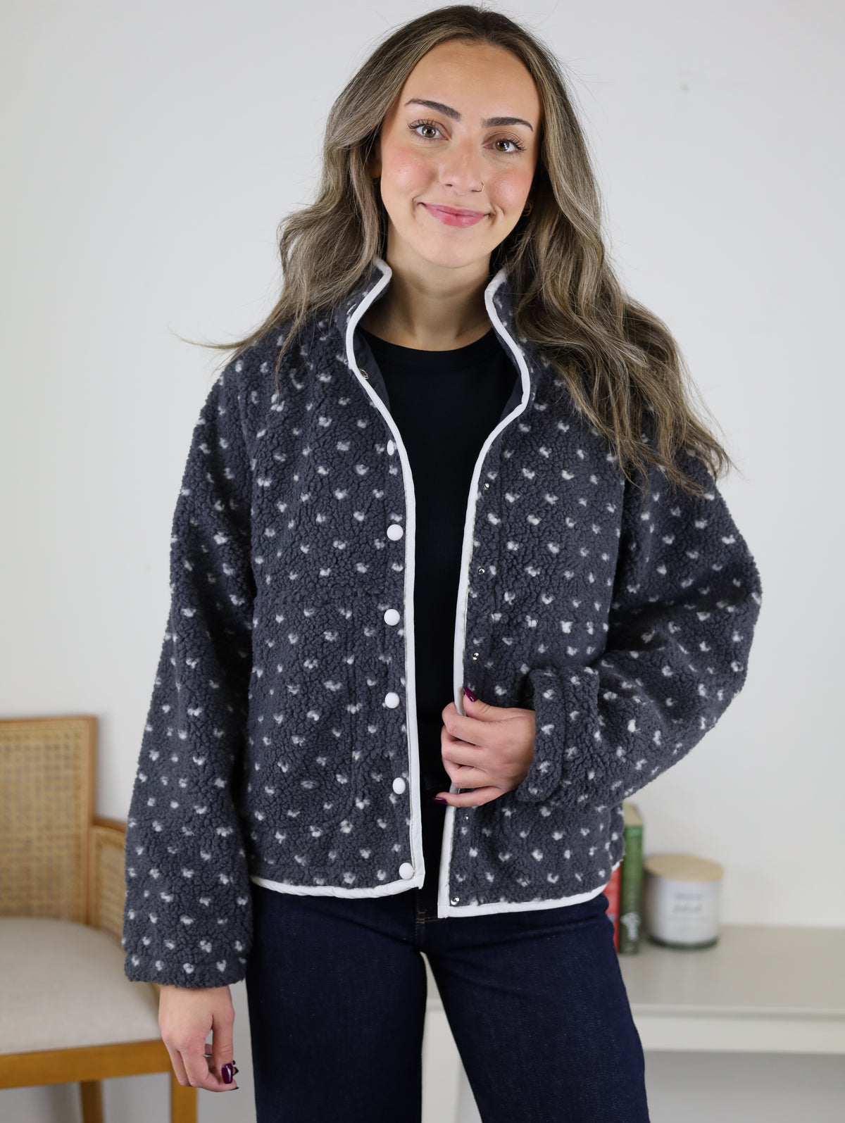 A woman wearing the charcoal grey Reba Fleece Puffer Jacket with a white heart pattern and white piping trim.