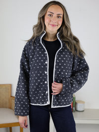 A woman wearing the charcoal grey Reba Fleece Puffer Jacket with a white heart pattern and white piping trim.