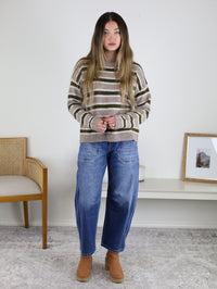 A person wears an Alexandria Striped Classic Sweater in mocha, tan, and olive green paired with wide-leg blue jeans and tan heeled boots.