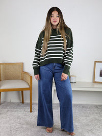 A person wearing a dark green and white Noa Striped Sweater in an oversized cotton knit paired with wide-leg blue jeans.