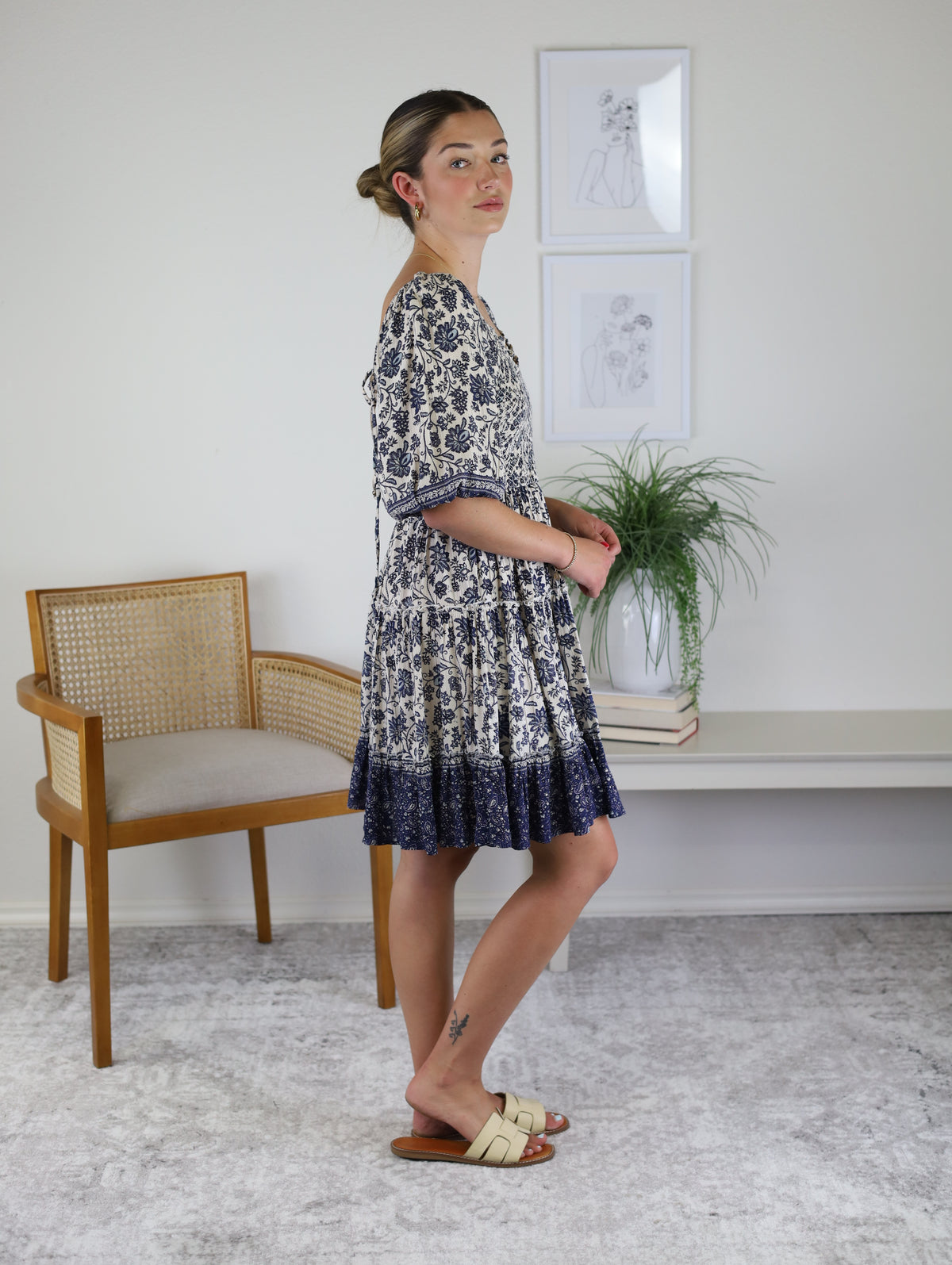 A woman wears the Leslie Smocked Mini Dress, featuring a blue and white floral pattern, a lace-up back, and a tiered skirt.