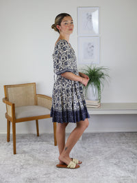 A woman wears the Leslie Smocked Mini Dress, featuring a blue and white floral pattern, a lace-up back, and a tiered skirt.
