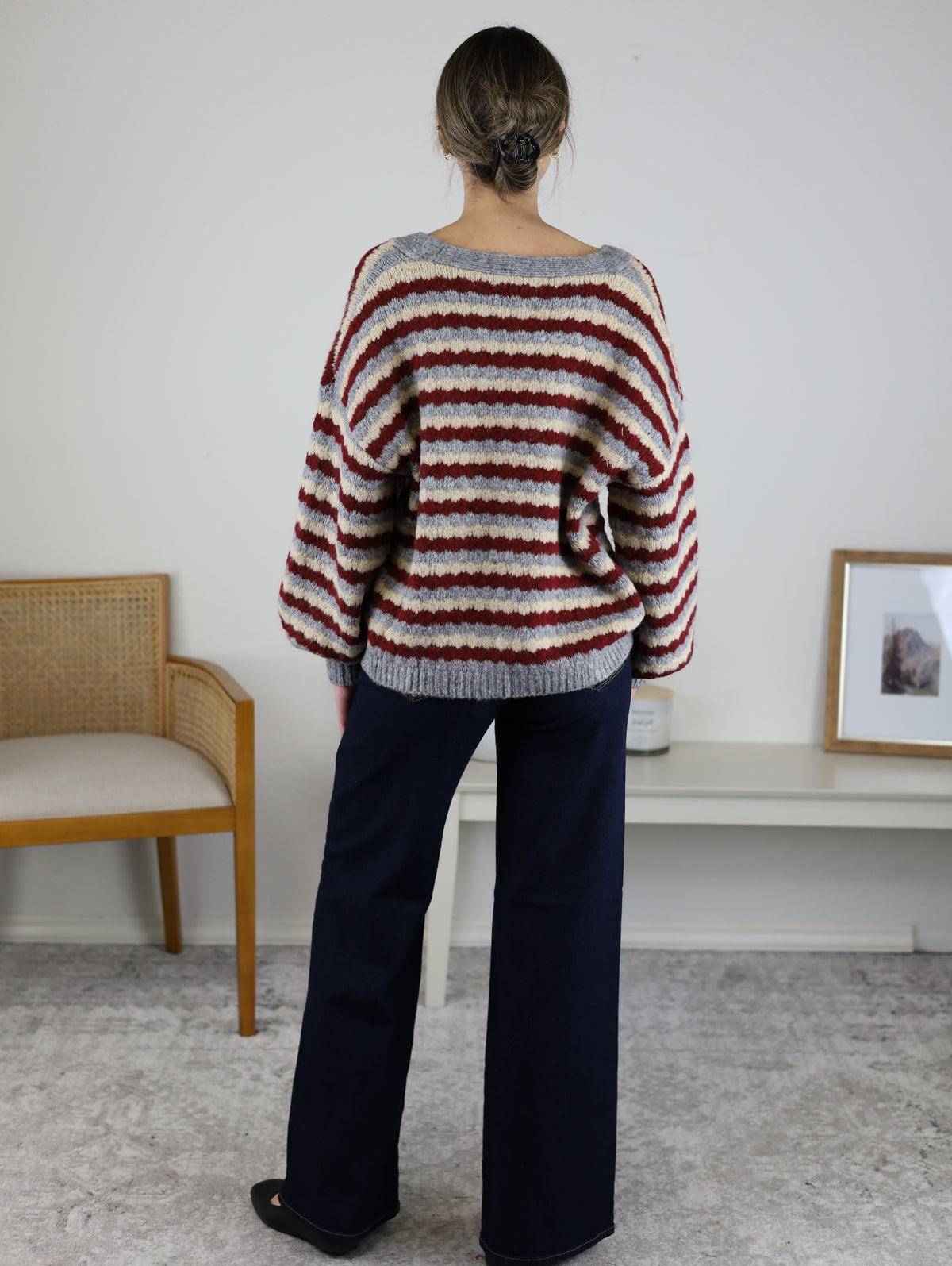 A person viewed from behind wearing a maroon, cream, and grey Grayson Relaxed Stripe V-Neck Button Cardigan paired with dark wide-leg jeans.