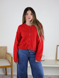 A person wearing a long-sleeved red Jude Raw Edge Cardigan and blue jeans.