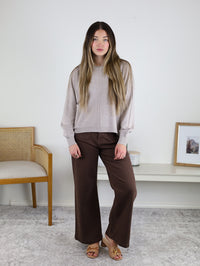 A woman wears an Eli Front Seam Sweater in beige viscose blend knit with a vertical front seam, paired with brown wide-leg pants.