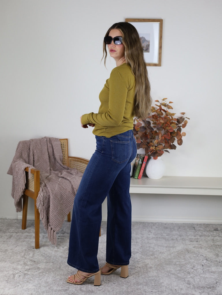 A woman wearing a dijon yellow Dee Ribbed Round Neck Tee, dark wash wide-leg jeans, and heeled sandals.