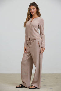 A woman stands indoors facing forward with a neutral expression, wearing the Creamon - CTP3592 BROWN Lounge Striped Button Down Top & Pants Set in brown stripe. The set features a button-down top and matching wide-leg pants with a drawstring waist, paired with black sandals.
