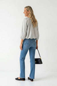 A woman wearing a light gray Naked Zebra - Elastic Puff Sleeve V-neck Blouse and blue jeans carries a black handbag.