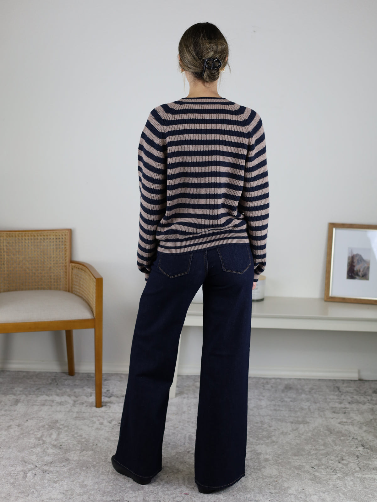 A person seen from behind wearing a Justine Longsleeve Crewneck Striped Sweater in tan and navy blue paired with dark wash wide-leg jeans.