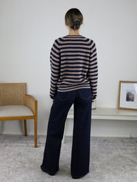 A person seen from behind wearing a Justine Longsleeve Crewneck Striped Sweater in tan and navy blue paired with dark wash wide-leg jeans.