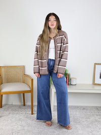 A person wearing a brown and white Nora Stripe Button Down Knit Cardigan over a white tank top with wide-leg blue jeans.