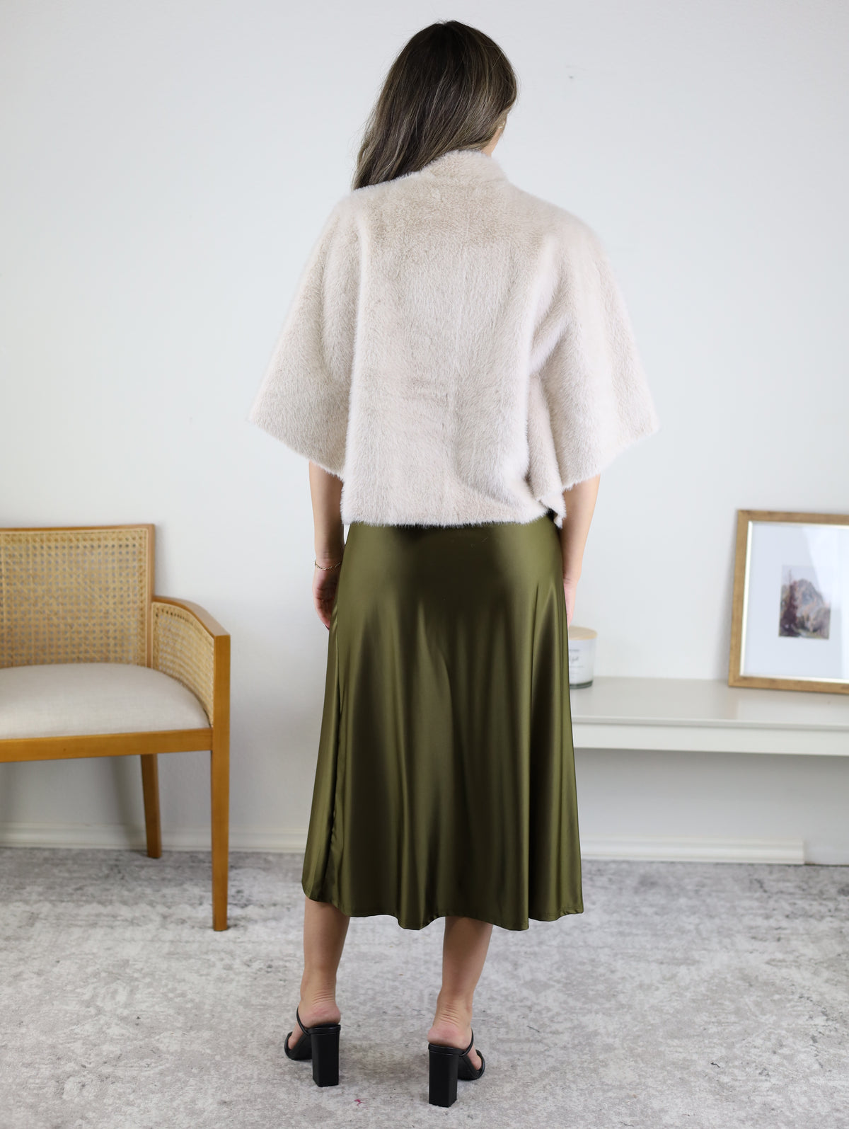 A person wearing a Jordan Fur Cape Sleeve Jacket over an olive green satin midi skirt and black block-heeled sandals.