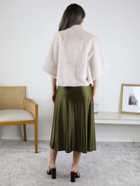 A person wearing a Jordan Fur Cape Sleeve Jacket over an olive green satin midi skirt and black block-heeled sandals.