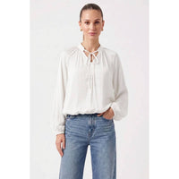 A woman wearing a white, billowy Naked Zebra - Billowy Tie Neck Long Sleeve Blouse tucked into blue jeans.