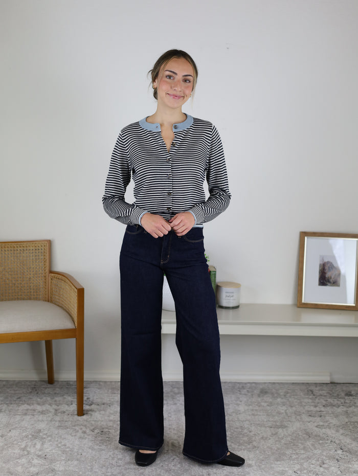 A woman wearing a Vera Striped Cardigan in a navy and white knit with light blue trim and dark wash wide-leg jeans, perfect for fall layering.