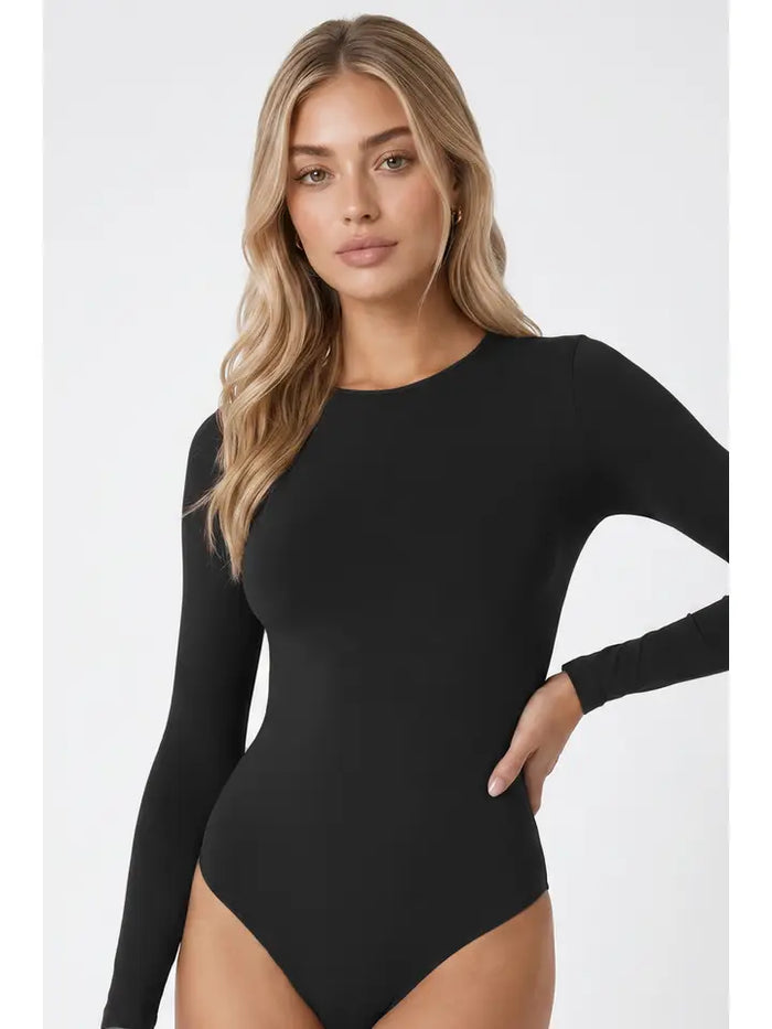 A woman with long blonde hair poses with one hand on her hip against a plain white background, wearing the High Neck LS Bodysuit—a fitted, long sleeve essential that’s perfect for layering in any season.