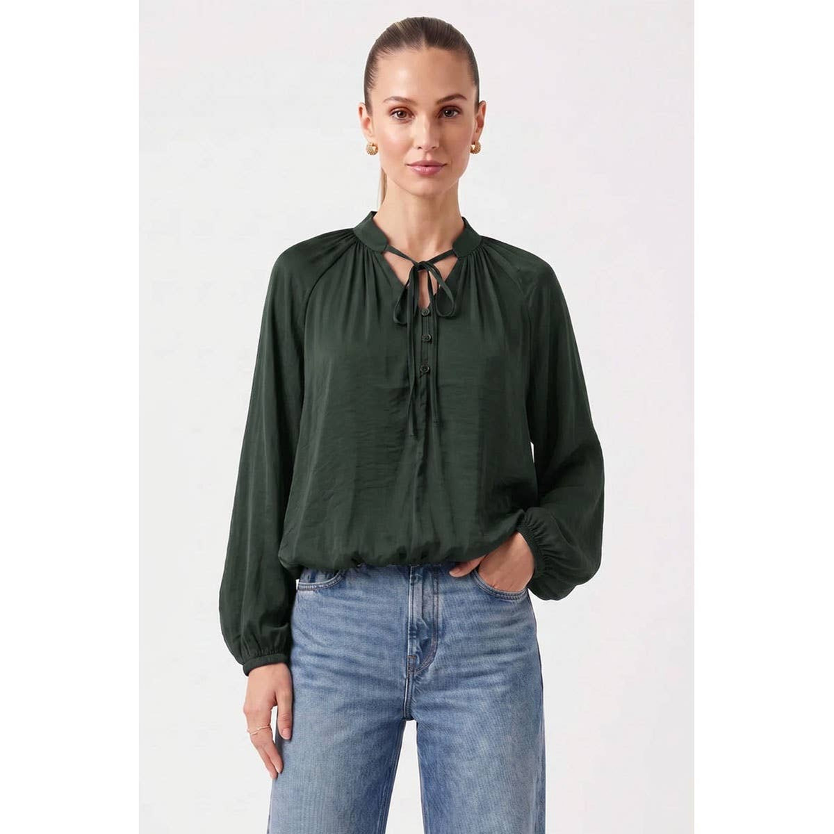 A woman wears a long-sleeved, dark green Naked Zebra - Billowy Tie Neck Long Sleeve Blouse: Wine / L with a button-front placket, tucked into blue jeans.
