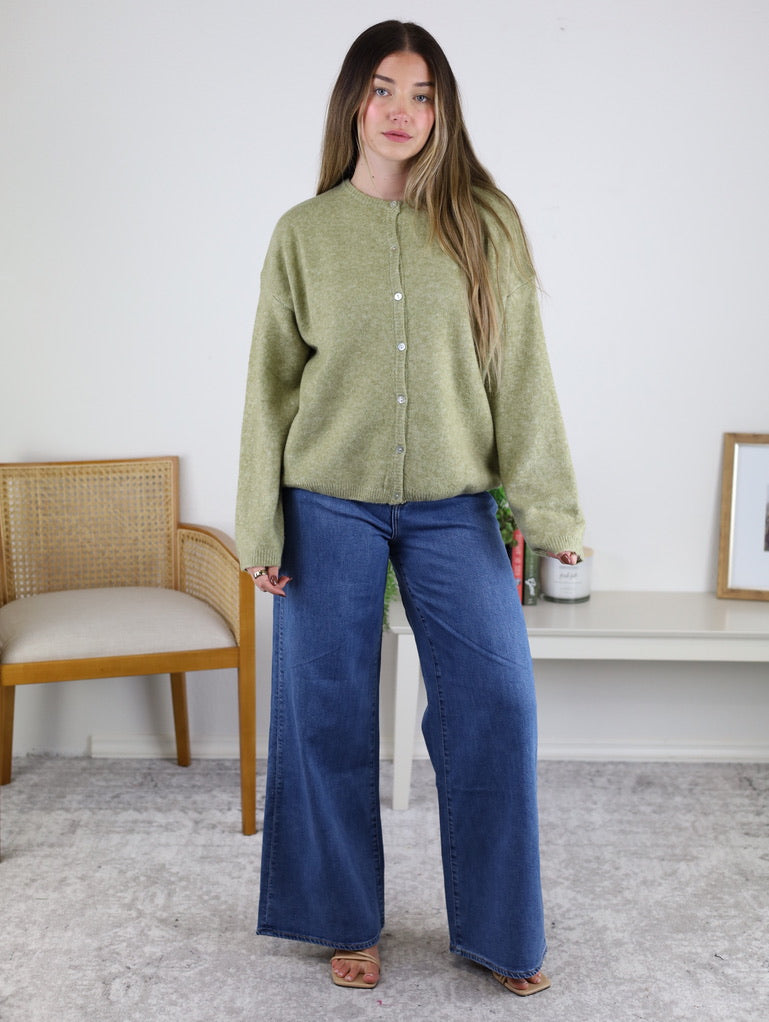 A woman wearing an Olive Oversized Cardigan in light green and wide-leg blue jeans.