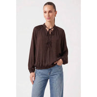 Woman wearing a wine Naked Zebra - Billowy Tie Neck Long Sleeve Blouse with a billowy fit, long sleeves, and an elasticized hem, paired with blue jeans.