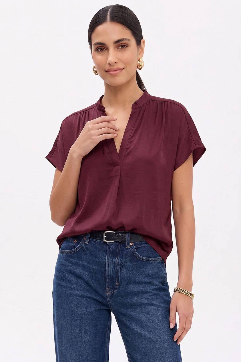 A woman wearing a dark red, short-sleeved Naked Zebra - Drop Shoulder Regular Blouse: Chocolate / L with a V-neckline and dark blue jeans.