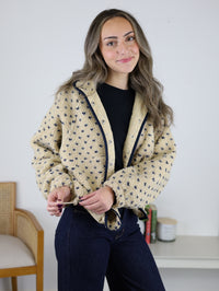 A woman wears a Reba Fleece Puffer Jacket in tan high-pile fleece with a cropped snap-front and navy blue star patterns, paired with a black top and dark jeans.