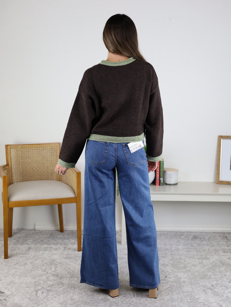 A person seen from behind wears a Maya Contrast Hem Cardigan in dark brown with light green trim at the neckline, cuffs, and hem, paired with wide-leg blue jeans.