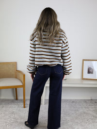 Viewed from behind, a person wears a Coastal Stripe Sherpa Striped Half Zip Pullover in blue and brown with dark blue wide-leg jeans.