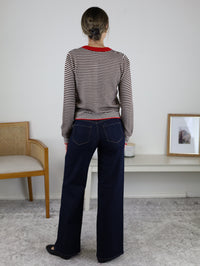 A person seen from behind wears a Vera Striped Cardigan featuring a brown and white striped lightweight knit with a red collar and hem, paired with dark blue wide-leg jeans.
