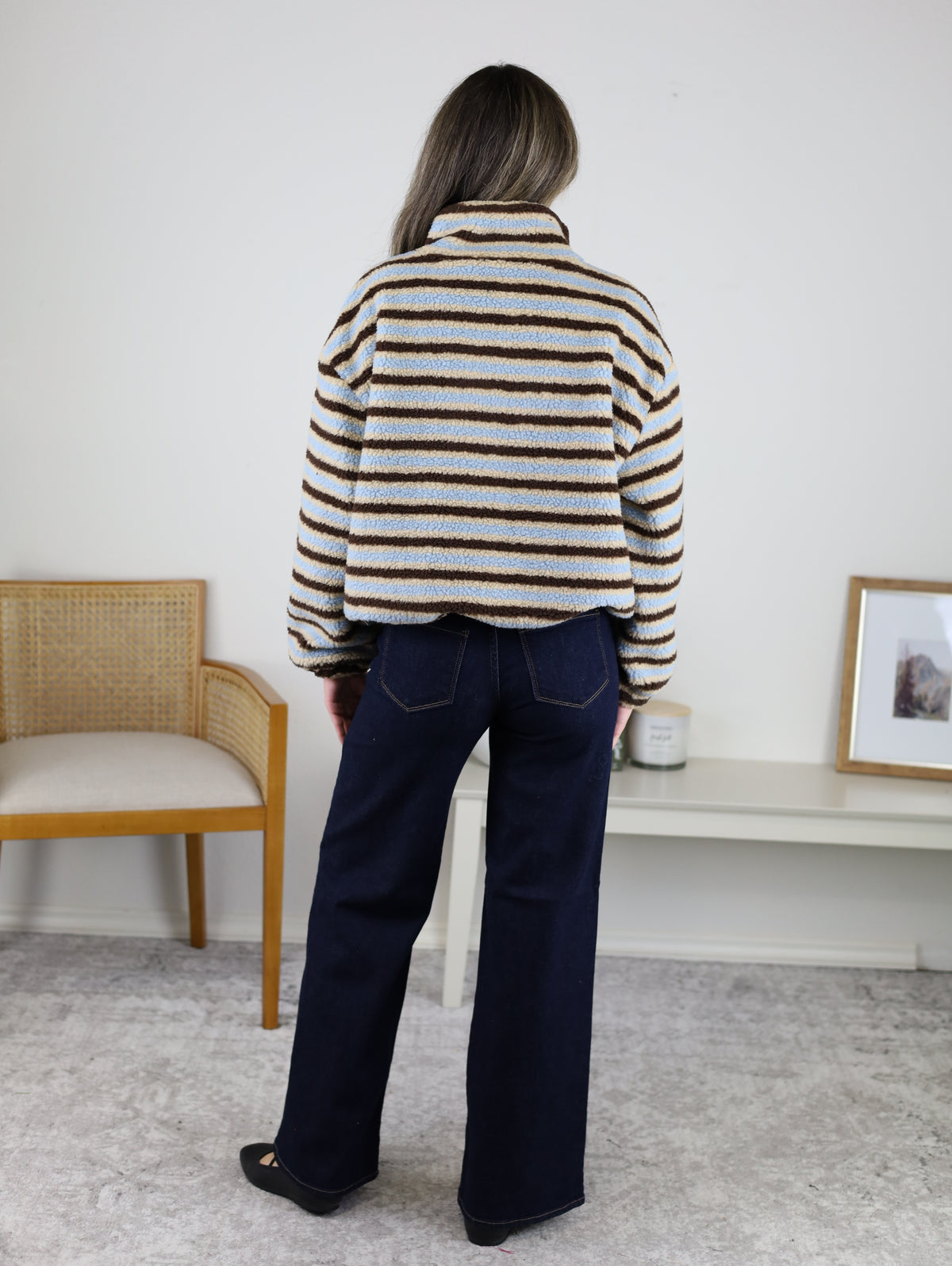 Back view of a person wearing a Coastal Stripe Sherpa Striped Half Zip Pullover with horizontal blue, tan, and brown stripes and dark-wash wide-leg jeans.