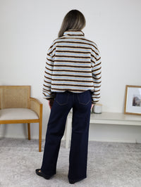 Back view of a person wearing a Coastal Stripe Sherpa Striped Half Zip Pullover with horizontal blue, tan, and brown stripes and dark-wash wide-leg jeans.