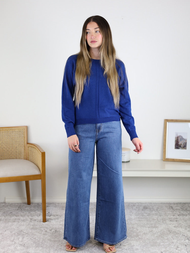 A woman wearing a royal blue Eli Front Seam Sweater in a viscose blend with a vertical front seam and wide-leg blue jeans.