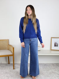 A woman wearing a royal blue Eli Front Seam Sweater in a viscose blend with a vertical front seam and wide-leg blue jeans.