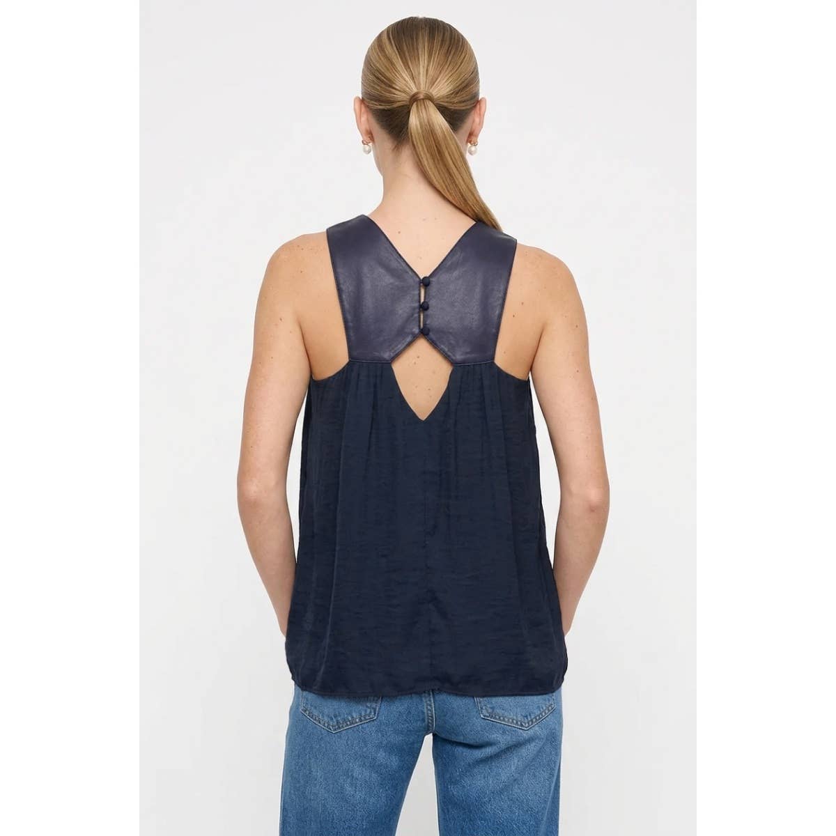 A woman seen from the back wearing a Naked Zebra - Vegan Leather Yoke Satin Tank: Wine / L, which is a navy blue satin tank top with a vegan leather yoke featuring two buttons at the nape of the neck.