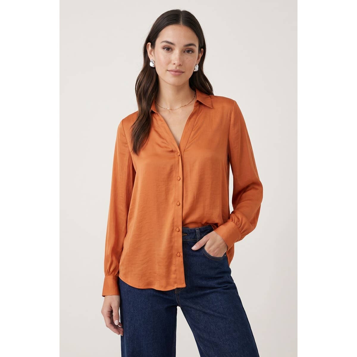 A woman wearing a Naked Zebra - Neck Shirt With Open Seam Sleeve in rust orange with open-seam sleeve details, paired with dark blue jeans.