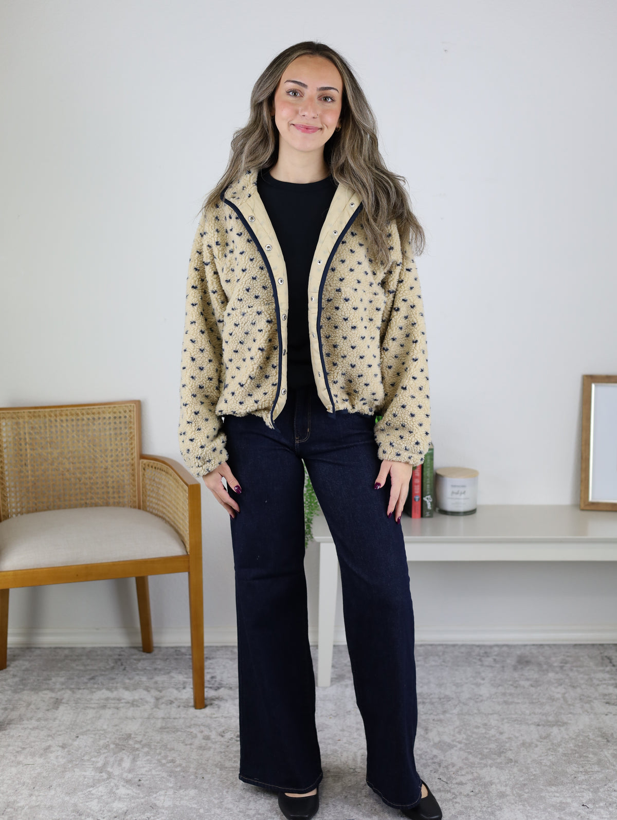 A person wearing a tan Reba Fleece Puffer Jacket with a small dark blue heart pattern, a black shirt, and wide-leg dark wash jeans.