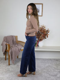 A person wearing a long-sleeved, ribbed terracotta Mindy Ribbed Striped Top and dark wash wide-leg jeans.