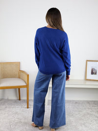 A person viewed from the back wearing a royal blue, round-neck viscose blend Eli Front Seam Sweater and wide-leg blue jeans.