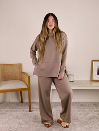 A woman wearing a taupe Arbor Lounge Set consisting of a matching long-sleeved top and wide-leg trousers.
