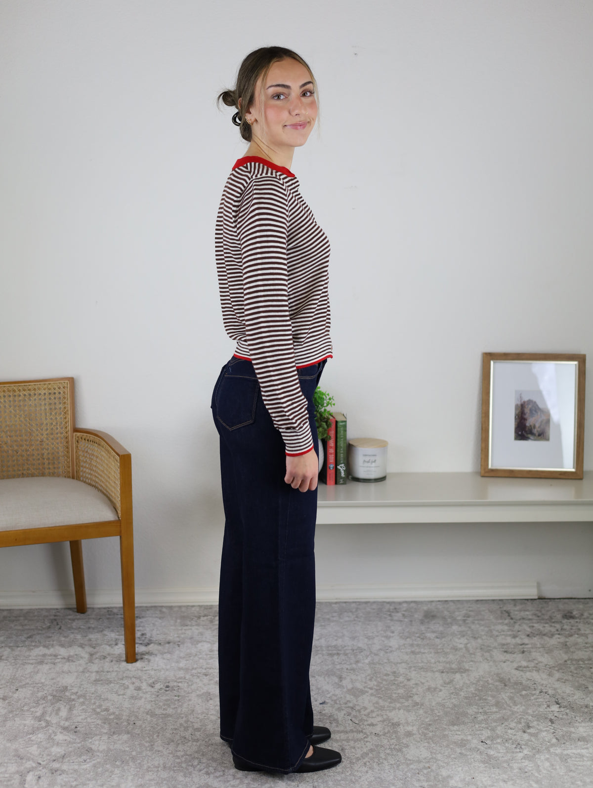 A person wearing a Vera Striped Cardigan in brown and white with red trim, paired with dark blue wide-leg jeans and black flats for fall layering.