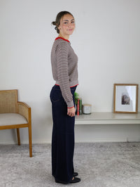 A person wearing a Vera Striped Cardigan in brown and white with red trim, paired with dark blue wide-leg jeans and black flats for fall layering.