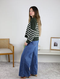 A woman wearing an oversized, dark green and white Noa Striped Sweater paired with wide-leg blue jeans.