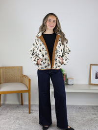 A woman wears a Casin Floral Print Fluffy Fleece Jacket with brown trim over a black top and dark-wash wide-leg jeans.