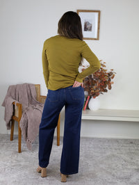 A person seen from behind, wearing a Dee Ribbed Round Neck Tee in olive green ribbed fabric and dark blue jeans, with one hand in their back pocket.