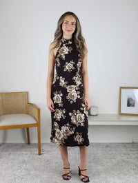 A woman wearing a brown floral Nash Halter Neck Midi Dress and black heeled sandals.