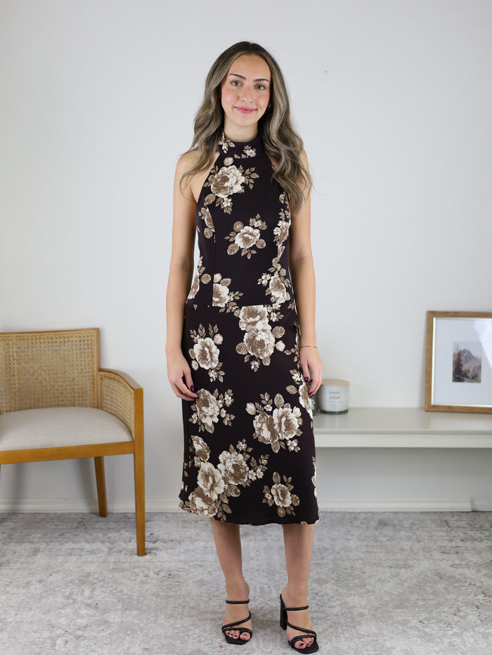 A woman wearing a brown floral Nash Halter Neck Midi Dress and black heeled sandals.