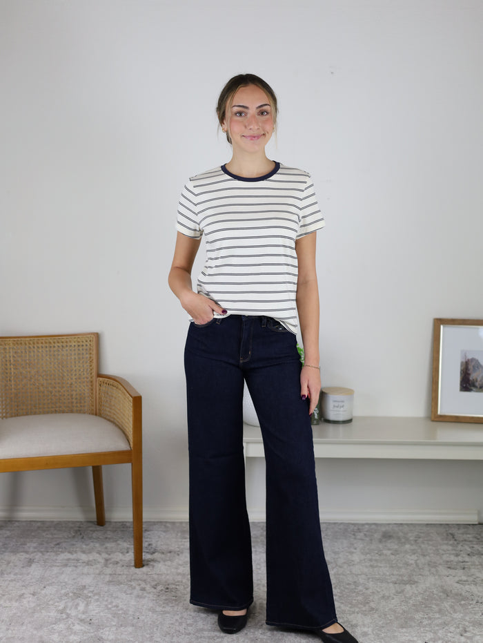 A woman wearing a classic crew neck striped short sleeve Asher Tee and dark-wash wide-leg jeans.