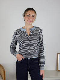 A woman wears a Vera Striped Cardigan, a lightweight knit with black and white stripes and light blue trim and buttons.
