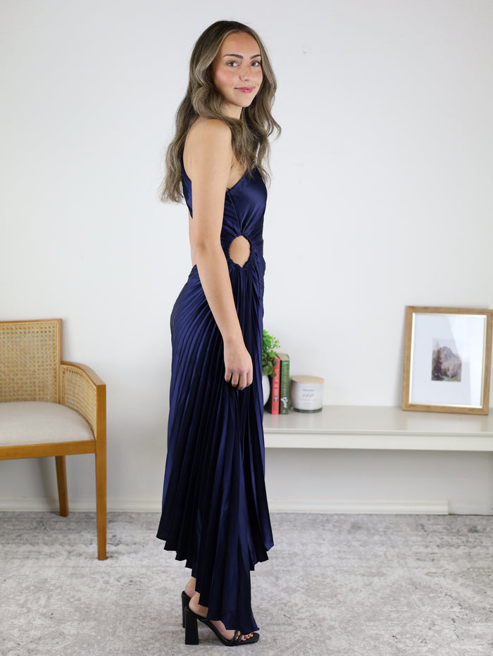 A person wears a dark blue Midi Satin One Shoulder Asymmetrical Pleated Dress with a side cutout and an asymmetrical hem.
