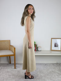 A person standing in profile wearing the tan, sleeveless suede Cole Suede A-Line Maxi Dress and black heeled sandals.